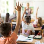 Back view of schoolboy raising hand to answer the question.